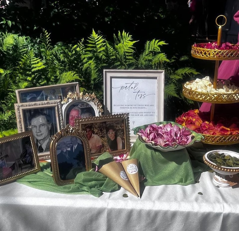 May include: A table decorated for a memorial service with a sign that reads "petal toss" in loving memory of those who are forever in our hearts. The table is decorated with flowers, photos, and small cones filled with petals.