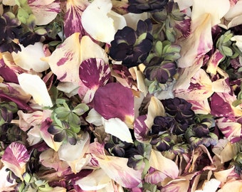 May include: A close-up of a mixture of dried rose petals in shades of white, cream, and pink with purple and green accents. The petals are scattered randomly and some are overlapping.