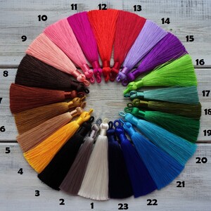 May include: A collection of colorful tassels arranged in a circular pattern. The tassels vary in color, including shades of pink, red, purple, green, and blue. Each tassel is approximately 10 cm long and has a loop at the top.