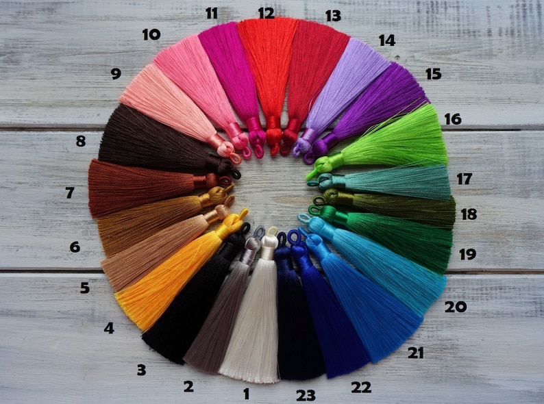 May include: A collection of colorful tassels arranged in a circular pattern. The tassels vary in color, including shades of pink, red, purple, green, and blue. Each tassel is approximately 10 cm long and has a loop at the top.