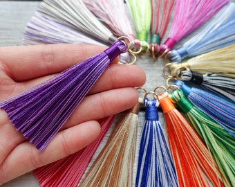 May include: A selection of colourful tassels with gold-coloured rings. A purple tassel is held, displaying its vibrant colour and texture. Other tassels in pink, green, and blue are arranged in a circle, offering a range of hues.