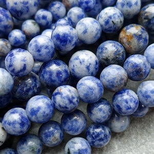 May include: A selection of blue sodalite gemstone beads with white marbling. The beads are of varying sizes and strung together, displaying a natural stone texture. Suitable for jewellery making.
