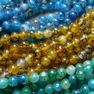 May include: Close-up of several strands of gemstone beads in shades of blue, yellow, and green. The beads have a cracked, textured appearance. These beads are suitable for jewelry making.