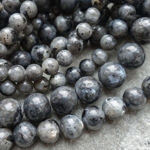 May include: A selection of grey labradorite beads, spherical in shape and of different sizes. The beads have a speckled appearance with hints of blue and black. Suitable for jewellery making, the beads are strung together.
