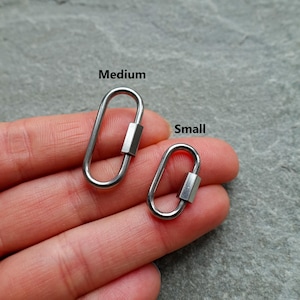 K&ouml;nnte beinhalten: Zwei ovale Karabinerhaken aus silberfarbenem Metall mit Schraubverschluss. Der gr&ouml;&szlig;ere Karabiner ist mit Medium und der kleinere mit Small beschriftet. Diese funktionalen Hardware-Komponenten verf&uuml;gen &uuml;ber eine glatte, polierte Oberfl&auml;che.