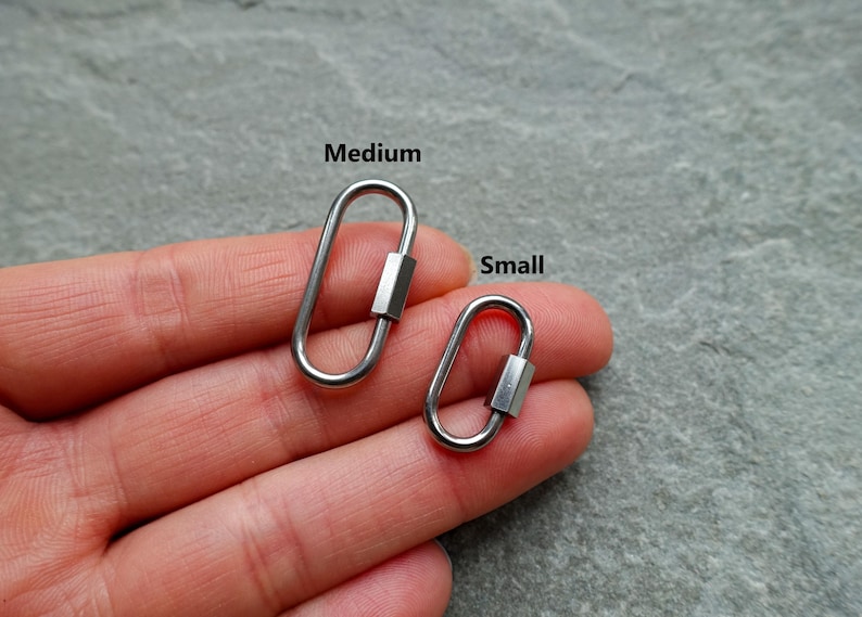 K&ouml;nnte beinhalten: Zwei ovale Karabinerhaken aus silberfarbenem Metall mit Schraubverschluss. Der gr&ouml;&szlig;ere Karabiner ist mit Medium und der kleinere mit Small beschriftet. Diese funktionalen Hardware-Komponenten verf&uuml;gen &uuml;ber eine glatte, polierte Oberfl&auml;che.