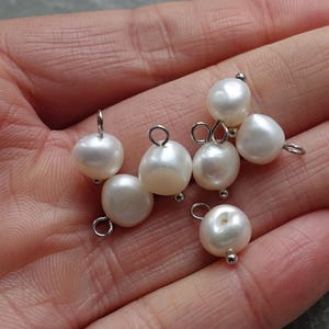 May include: A selection of white freshwater pearls, each with a silver-tone metal loop and a small ball. These pearls are suitable for jewellery making, providing a classic and elegant element to any design.