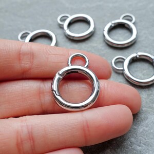 May include: A set of silver-toned metal spring gate rings, each featuring a circular main loop with a smaller attached loop at the top. The rings have a smooth, polished finish and a functional spring-loaded mechanism for opening and closing.