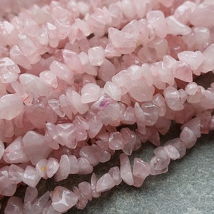 以下が含まれることがあります： ローズクォーツのチップビーズのストランドのクローズアップ。ビーズはソフトピンク色で、不規則な形をしています。ビーズはつながっており、質感のある表面を作り出しています。ジュエリー作りや工芸に最適です。