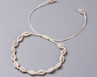 May include: A cream-coloured cowrie shell necklace and choker set. The necklace features multiple shells strung together, while the choker has a single shell at each end. The set is connected by a cream-coloured cord.