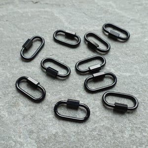 K&ouml;nnte beinhalten: Eine Ansammlung von neun kleinen, ovalen Federringen aus schwarzem Metall. Jeder Ring hat ein glattes, durchgehendes Design mit einem rechteckigen Federmechanismus an einer Seite, der ein sicheres &Ouml;ffnen und Schlie&szlig;en des Rings erm&ouml;glicht.