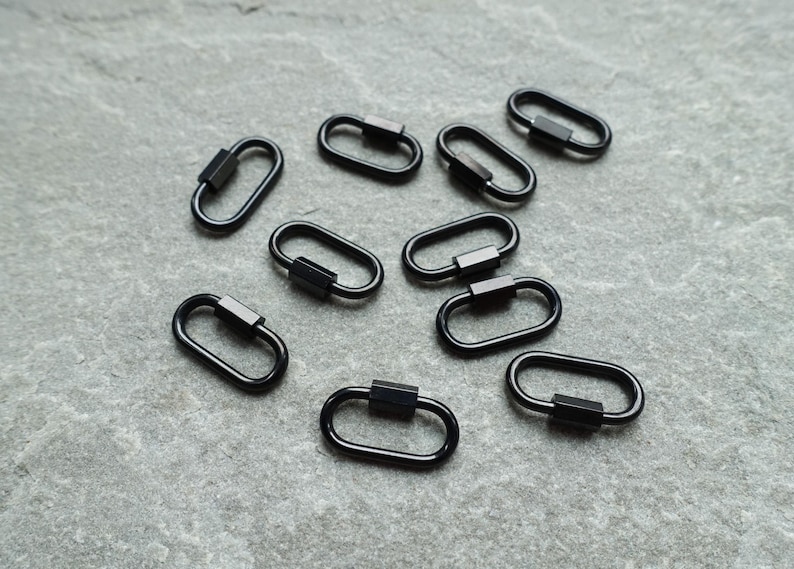 K&ouml;nnte beinhalten: Eine Ansammlung von neun kleinen, ovalen Federringen aus schwarzem Metall. Jeder Ring hat ein glattes, durchgehendes Design mit einem rechteckigen Federmechanismus an einer Seite, der ein sicheres &Ouml;ffnen und Schlie&szlig;en des Rings erm&ouml;glicht.