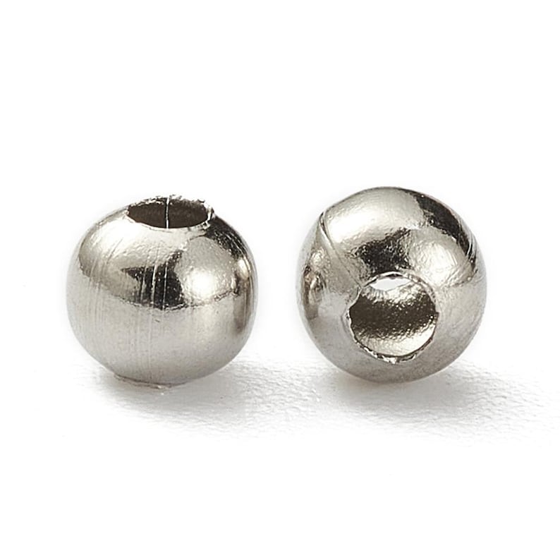 Peut inclure: Deux perles m&eacute;talliques argent&eacute;es brillantes avec une finition bross&eacute;e. Chaque perle est sph&eacute;rique avec un trou perc&eacute;. Ces perles sont probablement utilis&eacute;es pour la fabrication de bijoux ou d'autres travaux manuels.
