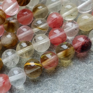 May include: Close-up of a collection of round beads in various colors, including clear, pink, and brown. The beads have a translucent quality, with internal patterns and inclusions. The beads are likely for jewelry making or crafting.