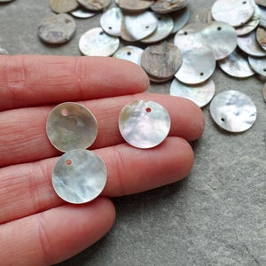May include: A collection of iridescent, round, mother-of-pearl shell beads. Each bead has a small hole for stringing. The beads vary in color, with shades of white, gray, and brown. These beads are ideal for jewelry making and craft projects.