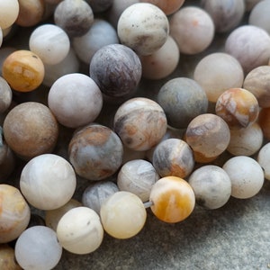 Può includere: Una collezione di perline rotonde in pietra naturale in varie tonalità di bianco, crema, marrone e grigio. Le perline hanno una finitura opaca e dimensioni variabili, creando un aspetto strutturato e organico. Ideale per la creazione di gioielli.