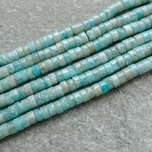 May include: Close-up of strands of turquoise gemstone beads. The beads are small, flat, and disc-shaped, with a mix of light and dark blue hues. The beads are strung together, creating a textured and colourful pattern, ideal for jewellery making.