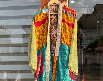 May include: A long, colorful kimono-style robe with a patchwork design. The robe is made of silk and has a variety of colors, including yellow, green, blue, pink, and purple. The robe is tied with a white sash and has a tag that says "93".