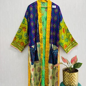 Könnte beinhalten: Ein langärmeliger Kimono-Bademantel mit Patchwork-Design und leuchtenden Paneelen in Blau, Limettengrün und Gelb. Das Kleidungsstück verfügt über zwei Vordertaschen, einen hellgelben Besatz mit Blattmustern und kleine reflektierende Spiegel.
