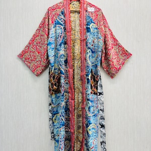 May include: A long, open-front robe with a vibrant paisley pattern in red, blue, and gold. The robe features wide sleeves and a matching belt. The garment is hanging on a wooden hanger against a neutral background.