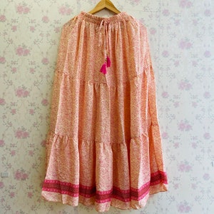 May include: A tiered maxi skirt with a pink and white floral print. The skirt has a drawstring waist and a pink tassel.