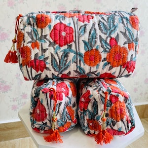 May include: Three stacked floral print fabric cosmetic bags with orange and pink flowers on a white background. The bags have a zipper closure and a tassel pull.
