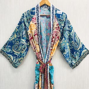 Peut inclure: Un peignoir kimono à manches longues arborant un motif cachemire multicolore vif dans des tons de bleu, jaune et rouge. Le vêtement présente une bordure blanche le long de l'ouverture avant avec un imprimé décoratif bleu foncé et une ceinture.