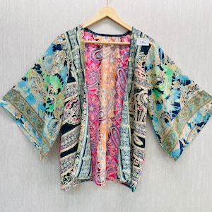May include: A vibrant kimono jacket with a paisley design in blue, green, pink, and orange. The open-front garment is suspended from a wooden hanger. The sleeves are wide and flowing, and the overall design is bright and eye-catching. The garment is a size 12.