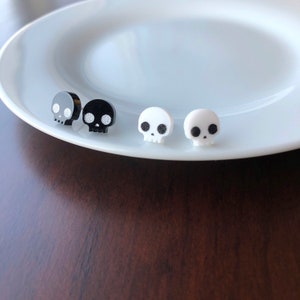 Two pairs of skull stud earrings.  One black pair and one white pair of stud earrings.