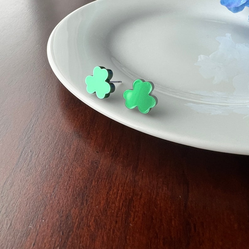 Pode incluir: Um par de brincos de bot&atilde;o verde em forma de flor em um prato branco. Os brincos s&atilde;o pequenos e delicados.