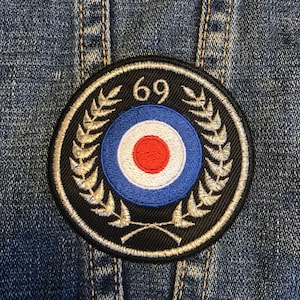 May include: A black and white embroidered patch with a red, white and blue target design. The target is surrounded by a silver laurel wreath and the number "69" is at the top.