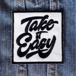 May include: White square patch with black embroidered text that reads "Take it Easy" in a stylized font.