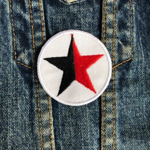 May include: A white, round patch with a black and red star. The star is divided in half, with the top half red and the bottom half black.