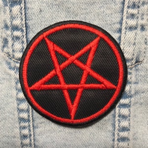 Può includere: Un cerotto circolare nero con un pentagramma rosso ricamato. Il cerotto è cucito su un tessuto di jeans blu.