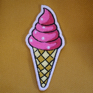 Puede incluir: Parche bordado de cono de helado rosa y blanco. El helado es rosa con puntos blancos y el cono es amarillo y marrón.