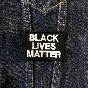 Op de afbeelding: Een zwarte patch met de tekst "Black Lives Matter" in wit op een spijkerjack.