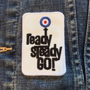 May include: White patch with black text that reads "ready steady go!" with a blue and red target symbol above the text.