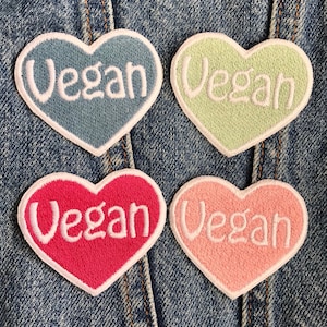 May include: Four heart-shaped patches with the word "Vegan" embroidered in white on each. The patches are in different colors: blue, green, pink, and red.