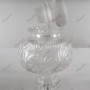 May include: A clear glass bottle with a textured surface and a decorative lid. The bottle has a round body and a wide base.