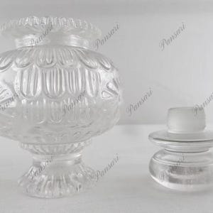May include: Two clear glass bottle stoppers with intricate designs. The larger stopper has a round, textured body with a wide base. The smaller stopper has a round, smooth body with a flat base.