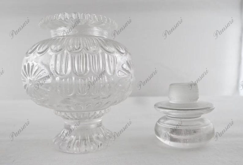 May include: Two clear glass bottle stoppers with intricate designs. The larger stopper has a round, textured body with a wide base. The smaller stopper has a round, smooth body with a flat base.