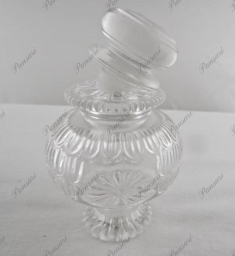 May include: A clear glass jar with a decorative, textured design. The jar has a lid with a unique, twisted shape.