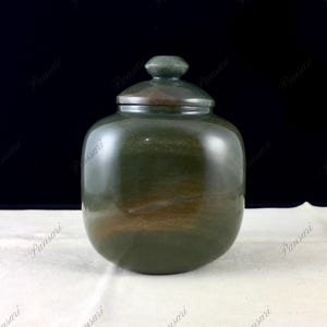 Puede incluir: Un tarro de piedra verde y marrón con tapa. El tarro es redondo y tiene una superficie lisa. La tapa también es redonda y tiene una superficie lisa.