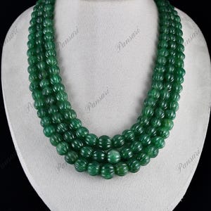 Op de afbeelding: Een meerstrengs ketting gemaakt van groene edelsteen kralen. De kralen zijn rond en hebben een gegraveerd, getextureerd oppervlak. De ketting wordt getoond op een witte mannequinbuste.