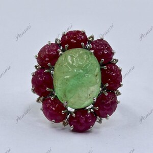 May include: A silver ring with a carved green gemstone surrounded by red rubies and diamonds.