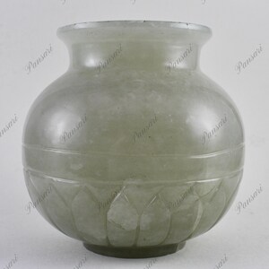 May include: A pale green, round, ceramic vase with a carved lotus design around the bottom.