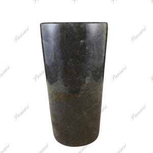 Puede incluir: Un jarrón cilíndrico gris oscuro hecho de piedra natural. El jarrón tiene una superficie lisa y pulida con sutiles variaciones de color y textura.