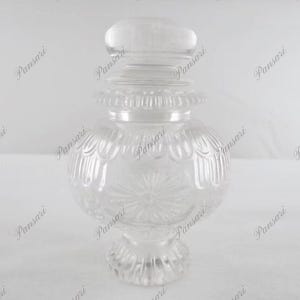 May include: A clear glass jar with a decorative lid and a textured design. The jar has a round body and a wide base.