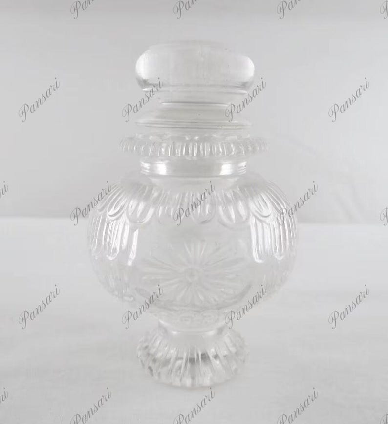 May include: A clear glass jar with a decorative lid and a textured design. The jar has a round body and a wide base.