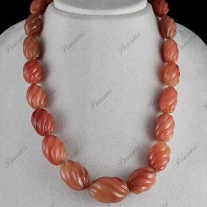 May include: A necklace made of carved carnelian beads. The beads are a deep orange colour and have a swirling pattern. The necklace is on a white background.